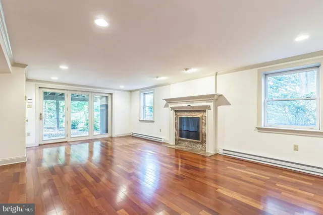 an empty room with wooden floor fireplace and windows