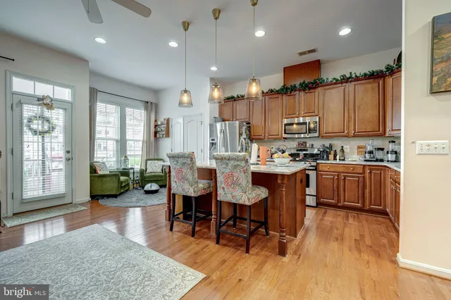 a kitchen with stainless steel appliances kitchen island granite countertop a refrigerator a stove a sink a dining table and chairs with wooden floor