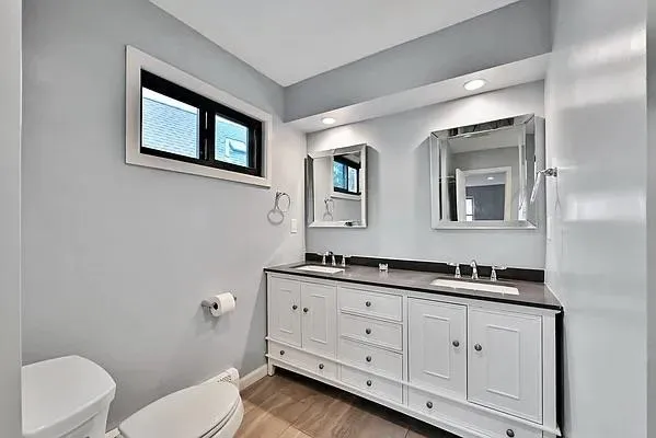 a bathroom with a toilet a double vanity sink and a mirror
