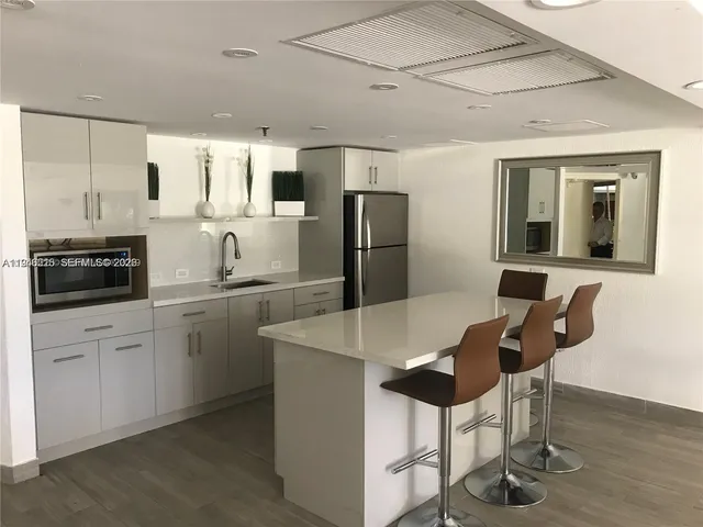 a kitchen with stainless steel appliances kitchen island granite countertop a refrigerator a stove a sink and white cabinets with wooden floor