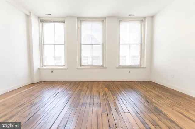 an empty room with wooden floor and windows