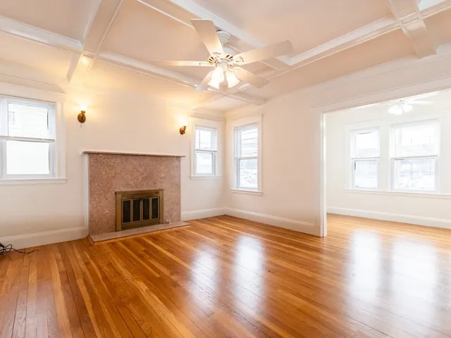 a view of an empty room with wooden floor fireplace and a window