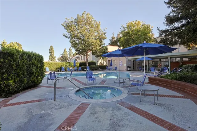 a patio with a dinning table and chairs under an umbrella with a fire pit and potted plants
