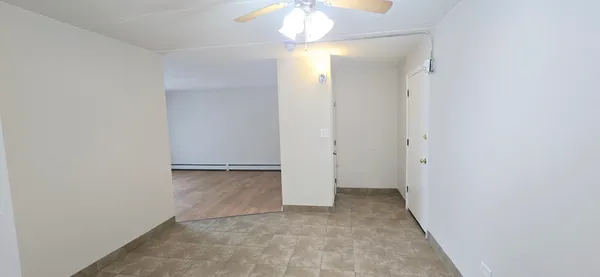 an empty room with a chandelier fan and kitchen view