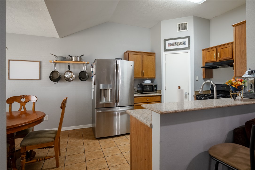 904 Crested Point Drive College Station, TX 77845 - Photo 4 of 11 Kitchen featuring stainless steel fridge, brown cabinetry, light tile patterned floors, a peninsula, and under cabinet range hood