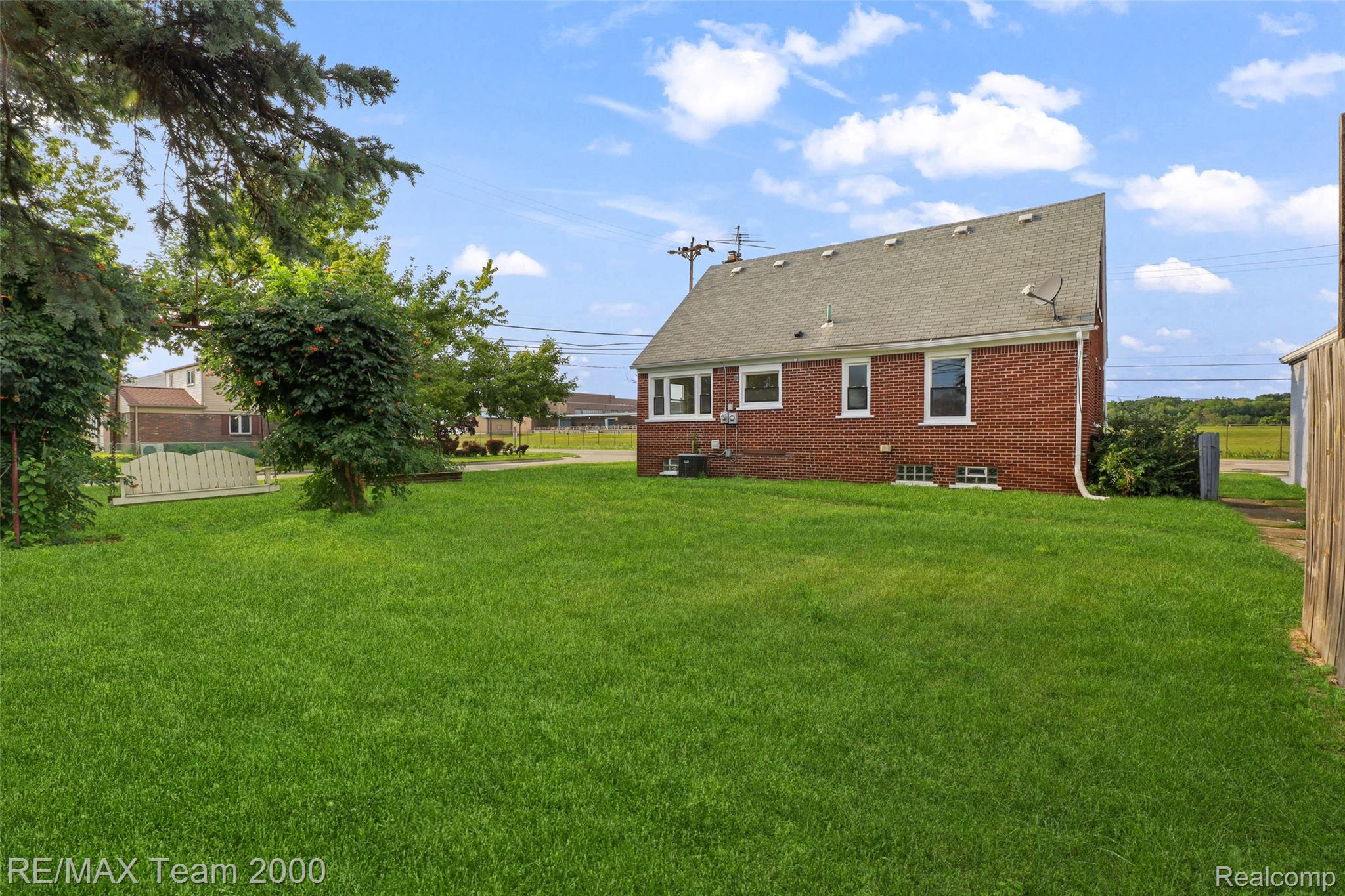 Expansive grassy backyard featuring a red brick exterior and a gabled roofline