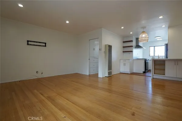 a view of empty room with wooden floor and kitchen
