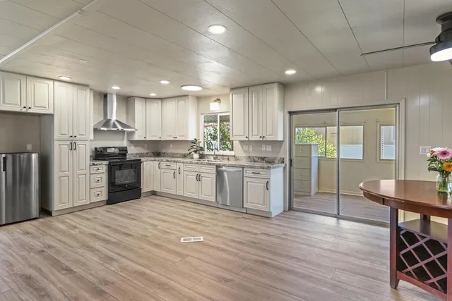 a kitchen with stainless steel appliances kitchen island granite countertop a refrigerator a sink dishwasher a stove and white cabinets with wooden floor