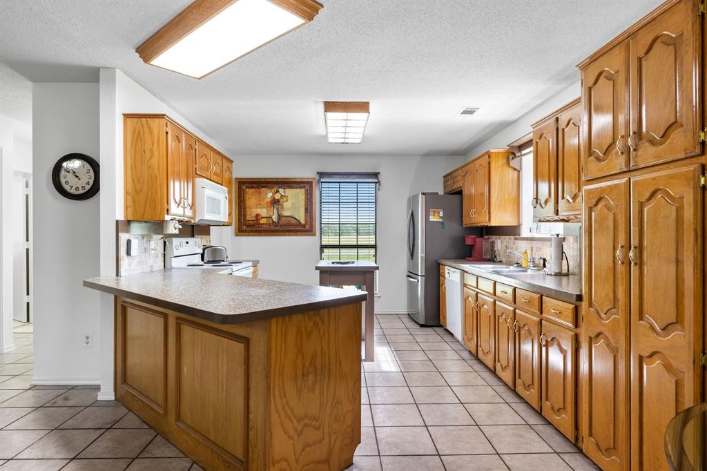 321 Vz County Road 2602 Wills Point, TX 75169 - Photo 15 of 39 Kitchen with white appliances, light tile patterned floors, brown cabinetry, a peninsula, and backsplash