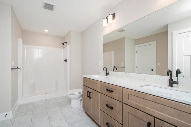 a bathroom with double sink a toilet a shower and a mirror