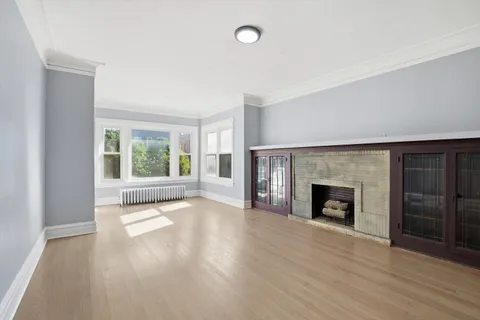 an empty room with wooden floor fireplace and windows