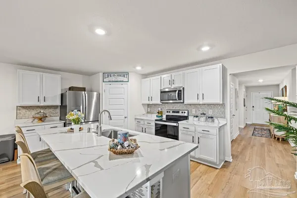 a kitchen with stainless steel appliances kitchen island granite countertop a stove a sink a refrigerator and white cabinets with wooden floor