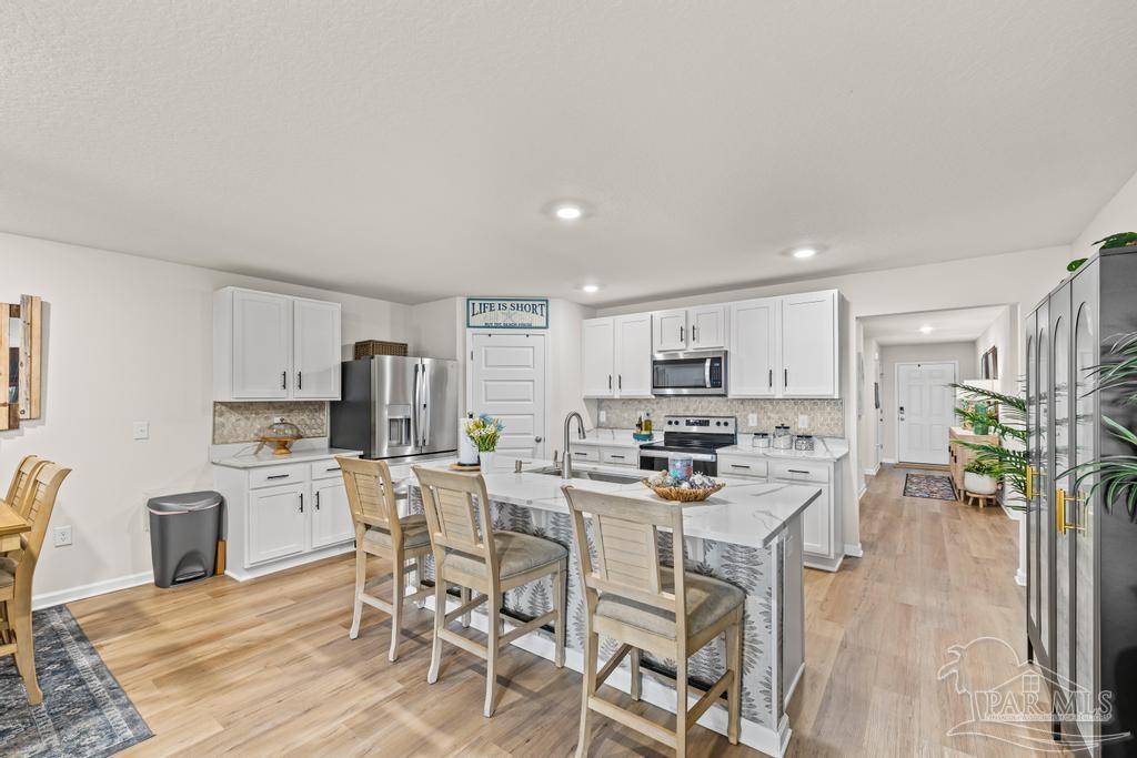 5277 Peach Drive Pace, FL 32571 - Photo 10 of 31 a kitchen with stainless steel appliances granite countertop a stove top oven a refrigerator a sink and a dining table with wooden floor