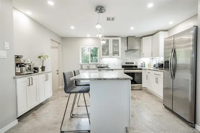 a kitchen with stainless steel appliances kitchen island granite countertop a stove a sink a refrigerator and white cabinets with wooden floor