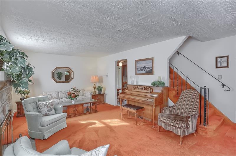 Enter the foyer and proceed into the spacious living room with original hardwood flooring beneath the carpeting.