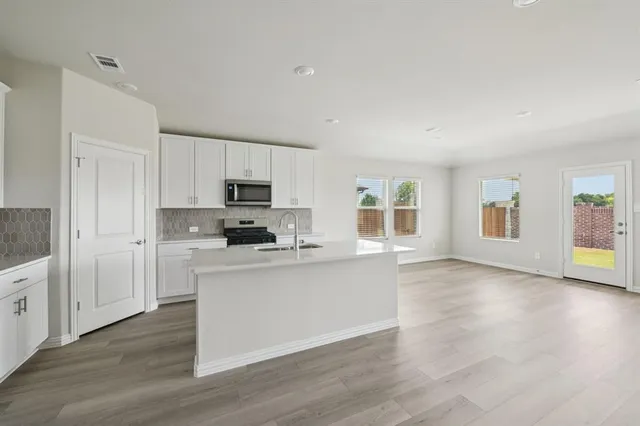 a kitchen with granite countertop a stove top oven a sink a refrigerator and white cabinets with wooden floor