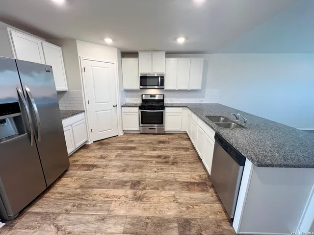 a kitchen with granite countertop a refrigerator a sink a stove top oven and wooden floor