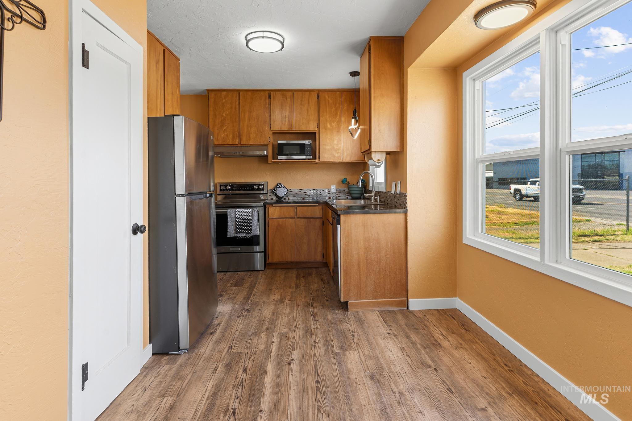 619 Thain Road Lewiston, ID 83501 - Photo 6 of 44 Kitchen featuring wood-finish flooring, light wood cabinetry, stainless steel appliances, and a tiled backsplash
