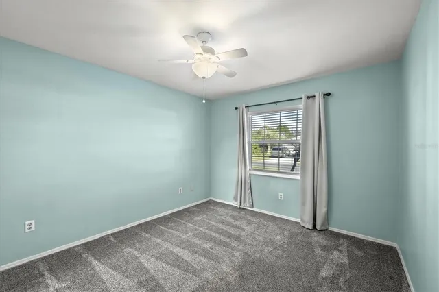 an empty room with chandelier fan and windows