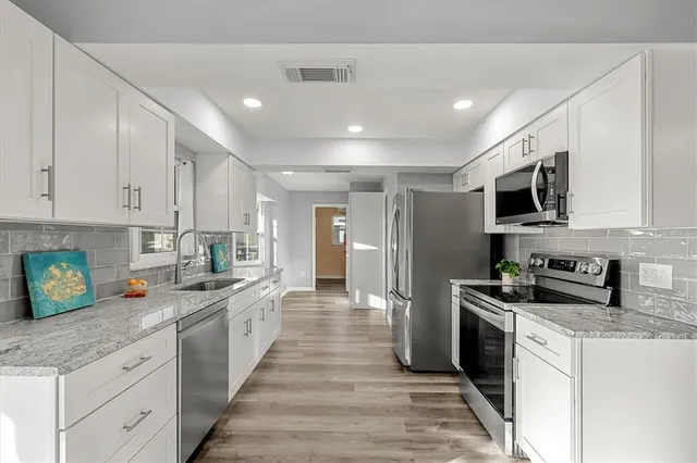 a kitchen with stainless steel appliances granite countertop a refrigerator a stove top oven a sink dishwasher and white cabinets with wooden floor