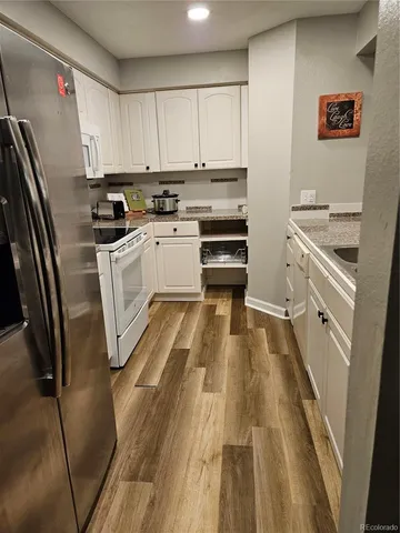 a kitchen with granite countertop a refrigerator a sink and white cabinets