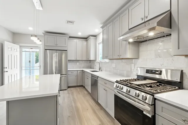 a kitchen with stainless steel appliances a white cabinets wooden floor and a window