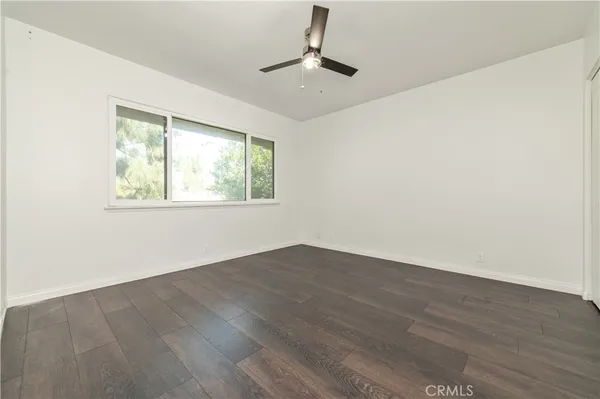 an empty room with wooden floor chandelier fan and windows