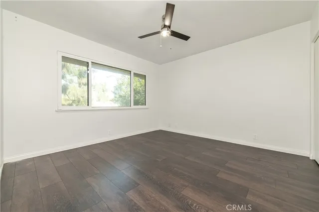 an empty room with wooden floor chandelier fan and windows
