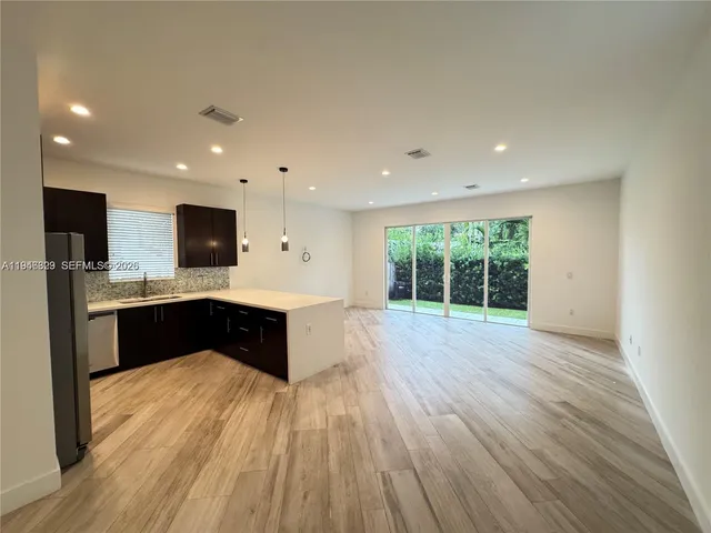 a large kitchen with stainless steel appliances granite countertop a large counter top a wooden floors and a large window