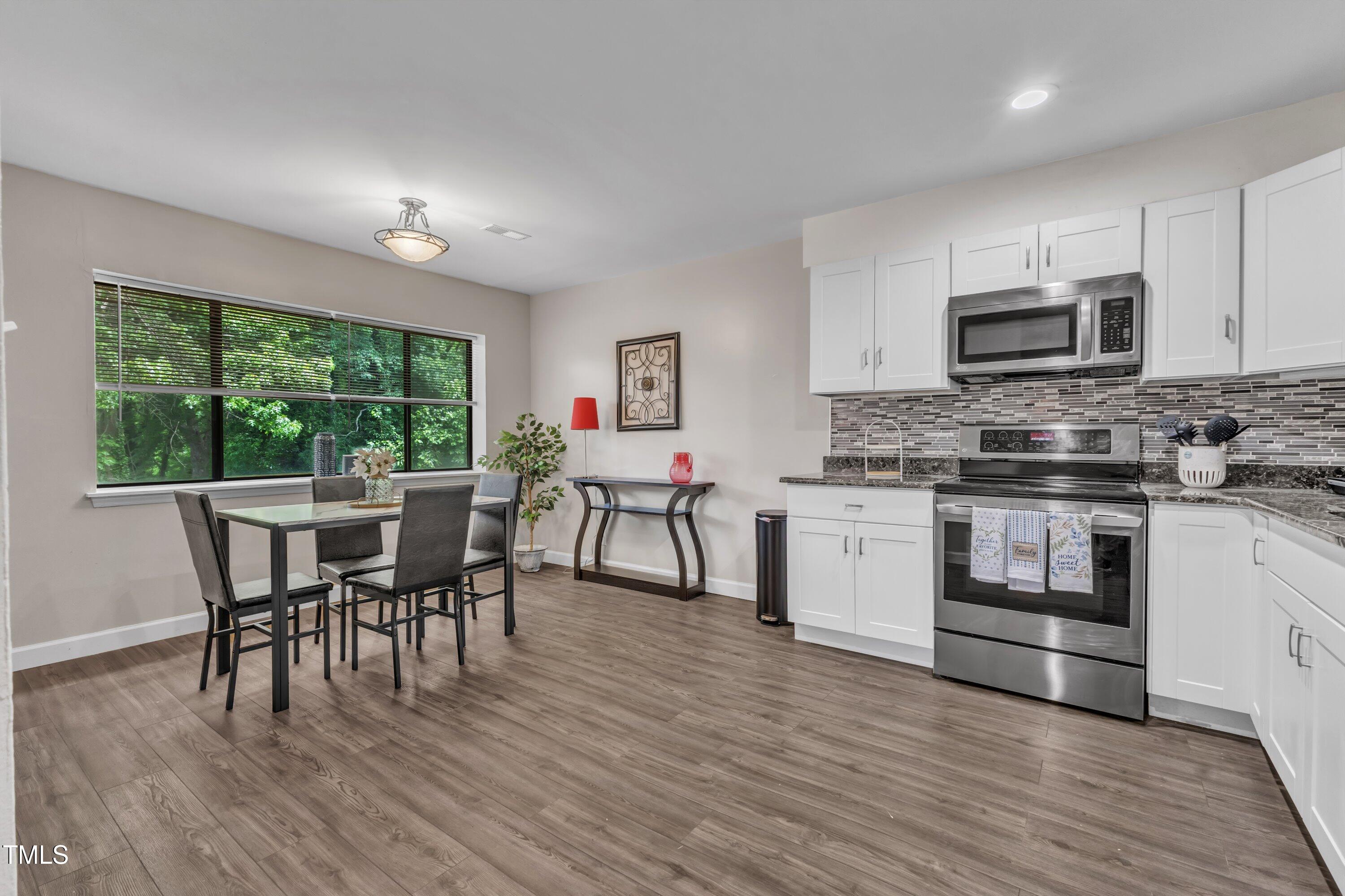 5022 Flint Ridge Place Raleigh, NC 27609 - Photo 6 of 32 a kitchen with stainless steel appliances granite countertop a stove a sink a microwave a dining table and chairs with wooden floor