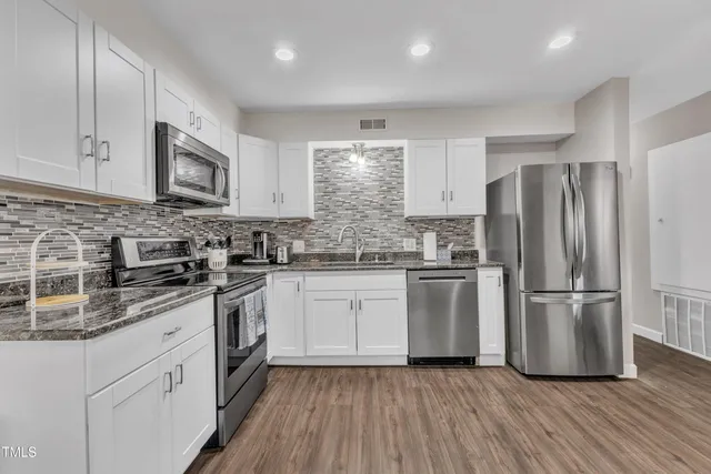a kitchen with stainless steel appliances granite countertop a refrigerator a stove a sink and white cabinets