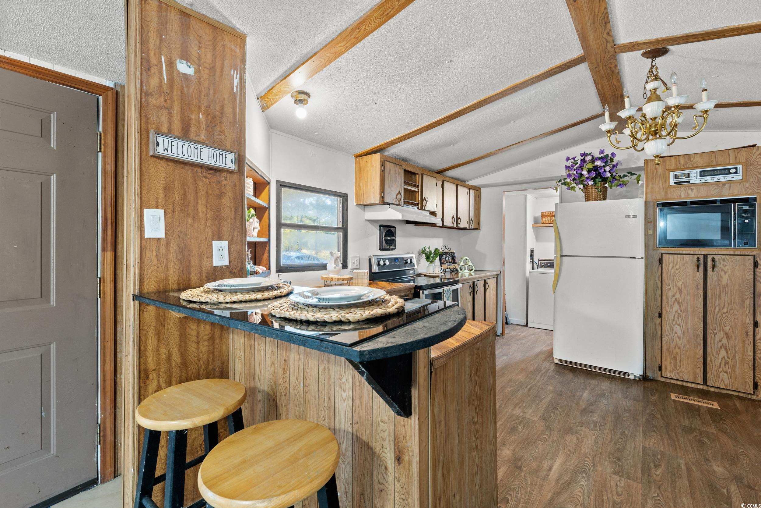 149 William Street Loris, SC 29569 - Photo 9 of 40 Kitchen featuring a kitchen breakfast bar, freestanding refrigerator, dark wood-style flooring, a peninsula, and a chandelier