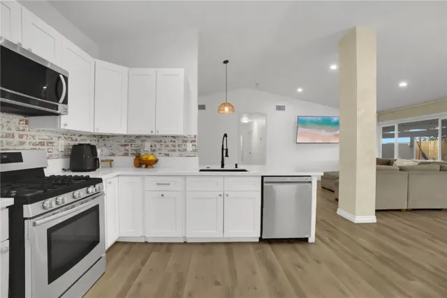 a kitchen with stainless steel appliances white cabinets a sink a stove a microwave and wooden floors