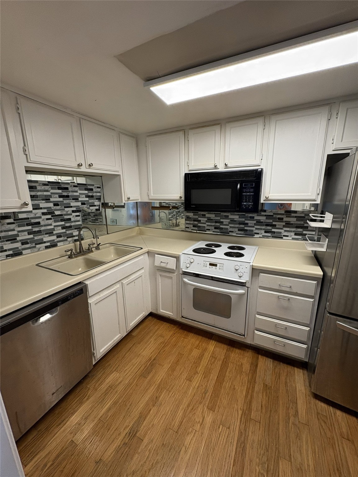 2016 Main Street, Unit 1620 Houston, TX 77002 - Photo 4 of 12 a white kitchen with granite countertop a stove top oven a sink and dishwasher a refrigerator with wooden floor