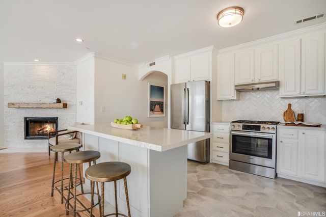 a kitchen with stainless steel appliances a stove a refrigerator a sink a dining table and chairs with wooden floor