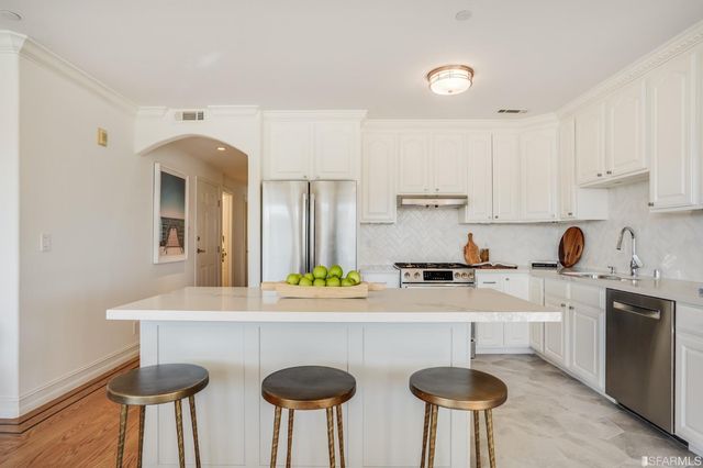 a kitchen with stainless steel appliances granite countertop a stove a sink a white cabinets and chairs