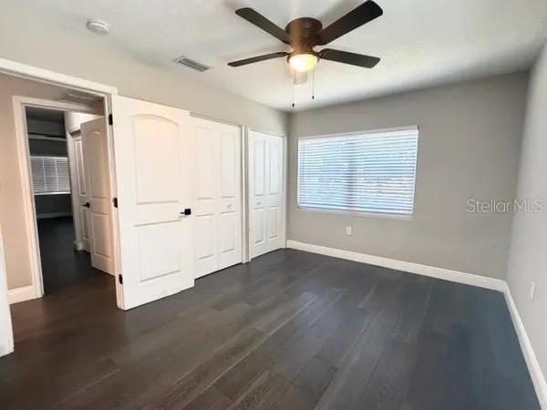 an empty room with wooden floor chandelier fan and windows