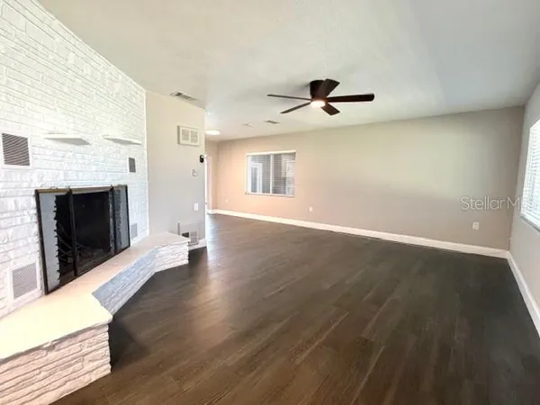 an empty room with wooden floor fireplace and windows