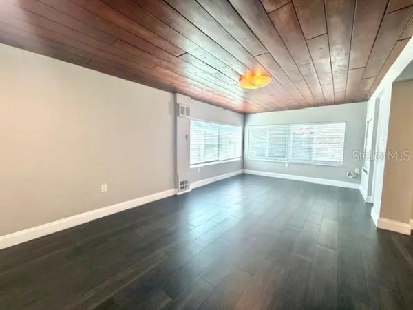 an empty room with wooden floor and windows with curtains
