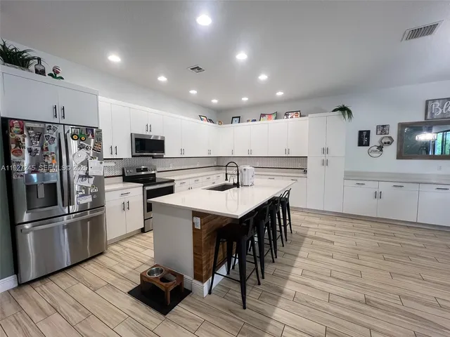a kitchen with stainless steel appliances kitchen island granite countertop a refrigerator oven a sink dishwasher and white cabinets with wooden floor