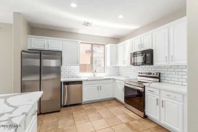 a kitchen with stainless steel appliances granite countertop a stove a sink dishwasher a refrigerator and a microwave oven with white cabinets