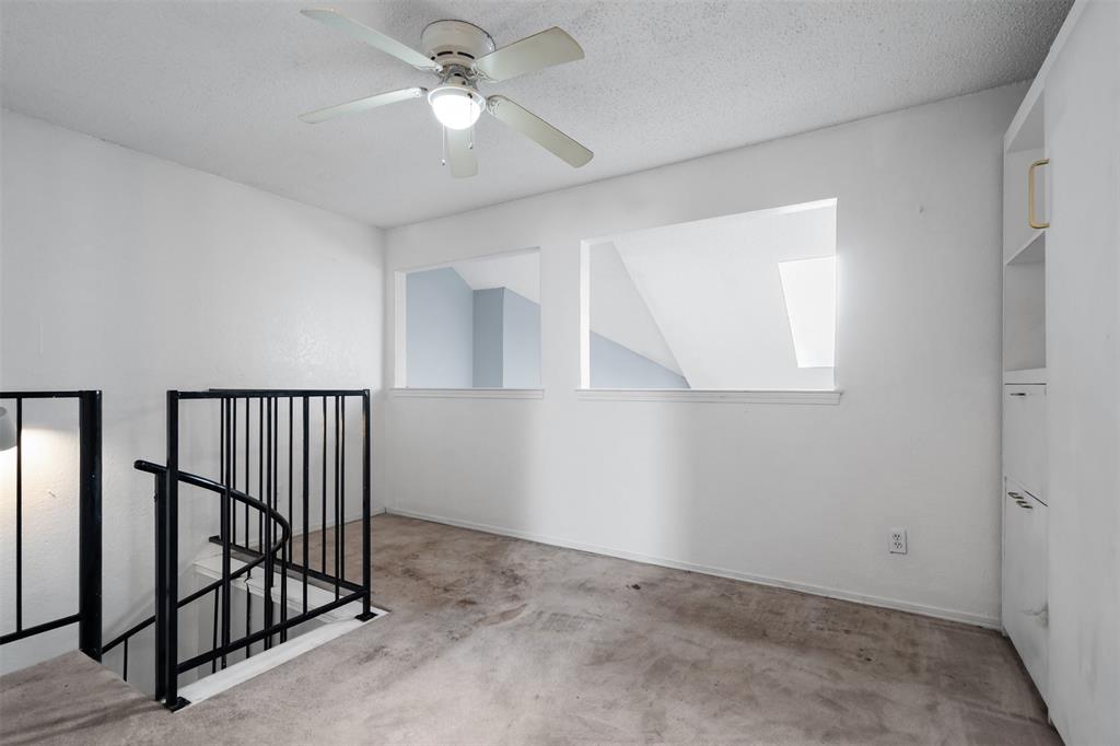 5590 Spring Valley Road, Unit H 203 Dallas, TX 75254 - Photo 22 of 27 Loft area featuring a ceiling fan with integrated lighting, built-in shelving, two interior windows, and a spiral staircase with black metal railing