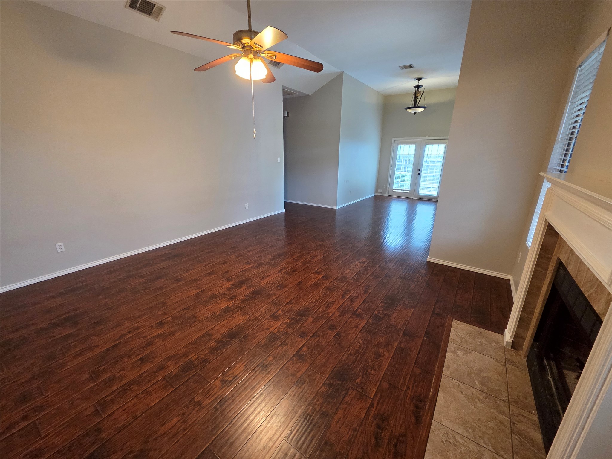 3001 Rochelle Drive Austin, TX 78748 - Photo 5 of 23 Unfurnished living room with dark wood-style floors, a ceiling fan, a tile fireplace, vaulted ceiling, and french doors