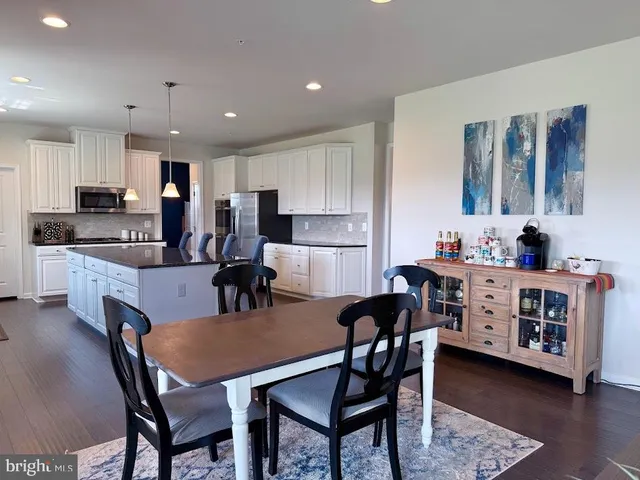 a large white kitchen with stainless steel appliances granite countertop lots of counter top space a refrigerator a stove a dining table and chairs with wooden floor