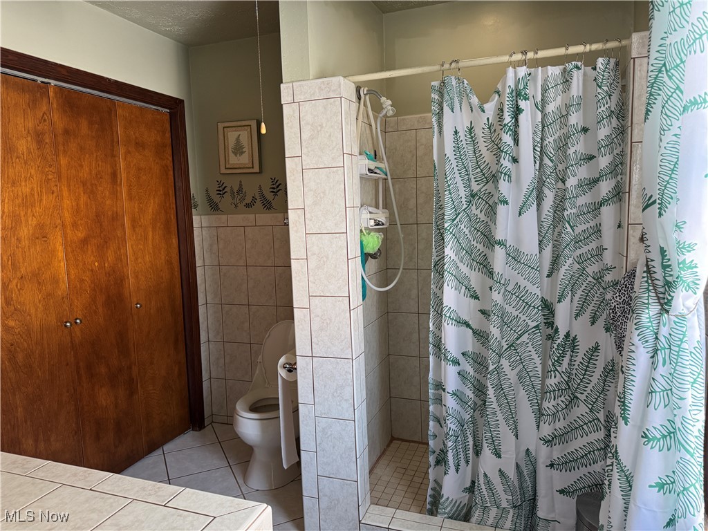 10004 Candy Road Cambridge, OH 43725 - Photo 9 of 20 Bathroom featuring a stall shower, light tile patterned floors, tile walls, and wainscoting