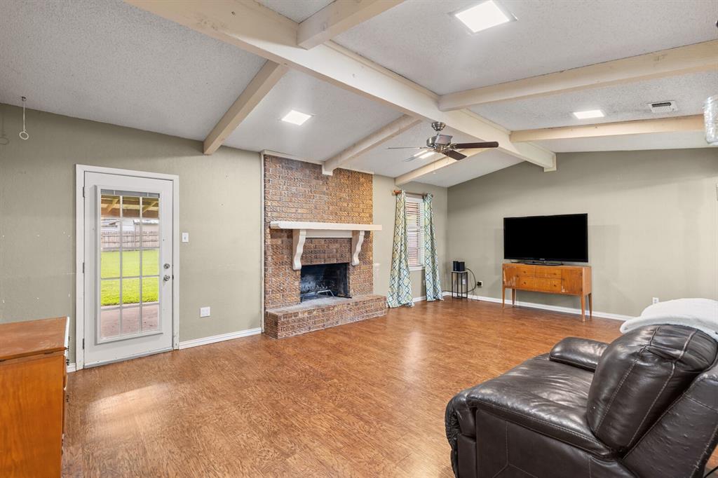 505 Pinewood Lane Hewitt, TX 76643 - Photo 15 of 38 Spacious living area featuring a vaulted ceiling with exposed beams, wood-finish flooring, a brick fireplace with a decorative mantel, and recessed lighting
