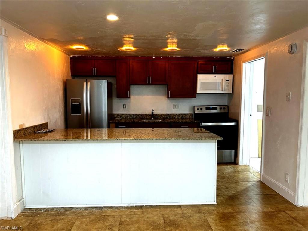 5324 Treetops Drive, Unit G2 Naples, FL 34113 - Photo 3 of 6 Kitchen with a peninsula, stainless steel appliances, dark stone counters, and reddish brown cabinets