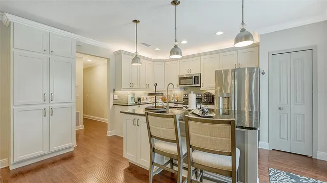 a kitchen with stainless steel appliances granite countertop a refrigerator a sink dishwasher a stove and white cabinets with wooden floor