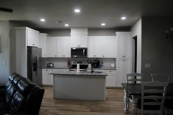 a kitchen with stainless steel appliances kitchen island granite countertop a refrigerator a stove a sink and a stove with wooden floor