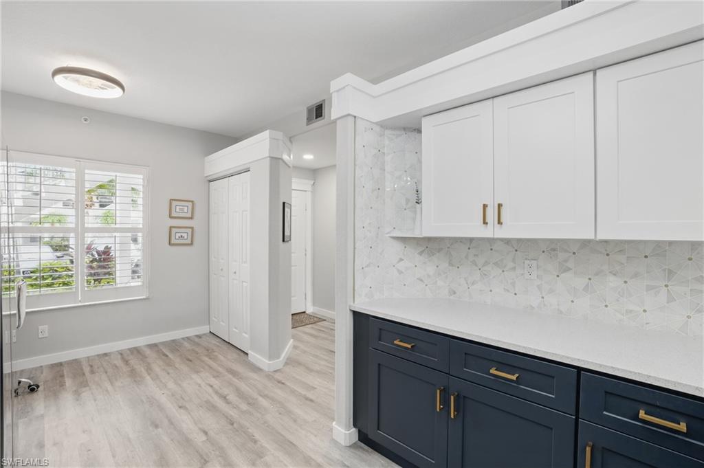 1220 Sarah Jean Circle, Unit L103 Naples, FL 34110 - Photo 16 of 50 Kitchen featuring white cabinetry, light countertops, backsplash, light wood-style floors, and baseboards